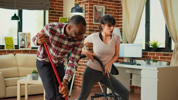 Diverse Couple Showing Dance Moves Having Fun Cleaning Apartment Using — Stock Photo, Image