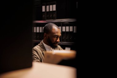 Özel dedektif polis kayıtlarında bilgi arıyor ve geç saatlere kadar çalışıyor. Polis elinde dosya dolu raflarla odada oturuyor. Dava dosyaları ve gece vakti suçları çözüyor.