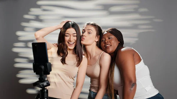 Group of interracial women having fun with photos, embracing imperfections and promoting self acceptance. Funny confident girl taking pictures on smartphone, body diversity in studio.