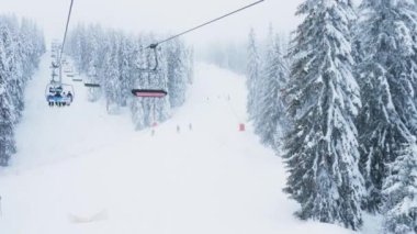 Pamporovo, Bulgaristan, Ocak 2023 - Ormanlarla çevrili buzlu dağın tepesine ulaşmak için profesyonel ekipman taşıyan kayakçılar kayak asansörü kullanıyorlar. Turistler dağlık tepelere tırmanıyor.