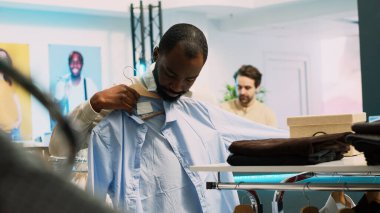 Erkek perakende müşteri raflardan kıyafet alıyor, indirimli almak için mağaza ürünlerine bakıyor. Müşteri olarak alışveriş merkezini ziyaret eden genç yetişkinler, ticari faaliyetler. El kamerasıyla..