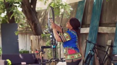 Aktif afro-amerikan kadın dikkatli bir şekilde gevşetiyor ve hasarlı bisiklet tekerleğini çıkarıyor. Spor düşkünü kadın bisikletçi, bakım için ön çataldan lastiği dikkatlice söküyor..