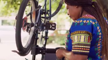 Afrika kökenli Amerikalı bayan bisikletçi hasarlı bisiklet lastiği lastiği üzerinde bakım yapıyor. Bisiklet parçalarını sıkmak için elinde tornavida tutan siyah kadının yakından görüntüsü.