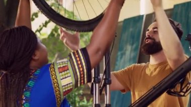 Sağlıklı Afro-Amerikan kadın, ev bahçesinde yeni bisiklet tekerleği için beyaz adamdan yardım alıyor. Spor düşkünü, çoklu etnik çeşitlilikte bir çift bisiklet lastiği takıyor..