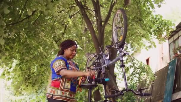 若い健康な黒人女性がプロのツールキットを調べ 自転車を修理しました 自宅の庭で損傷した自転車を修理するためのさまざまな専門機器を保持するスポーティな女性のサイクリスト — ストック動画