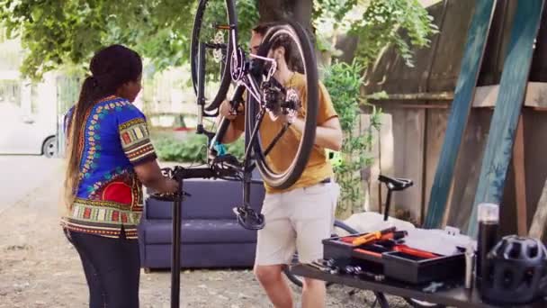 活跃的非洲裔美国女性咨询健康的高加索男性合适的工作工具 用于调整自行车踏板 多族裔夫妇在院子里谈论和维修现代自行车 — 图库视频影像
