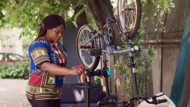 壊れた自転車の部品を修理するために必要な専門家ワークツールを準備する若い黒人女性 損傷した自転車を整備するためのスポーツ愛好の女性アレンジの異なる専門機器 — ストック動画