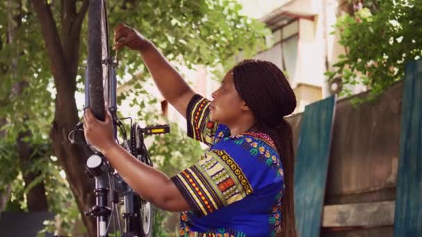 充满热情的运动非洲裔美国妇女紧固螺栓 并将轮子固定在自行车车架上 专用女骑手使用专用扳手拆卸外面损坏的自行车轮胎 — 图库视频影像