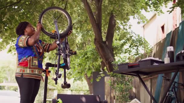 忠实的年轻女骑手在自家院子里小心地将轮胎与自行车架分开 健康的专用黑人妇女选择专用工具修理自行车零件 — 图库视频影像