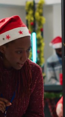 Noel Baba şapkası giyen dikey video çalışanı tablete fiyat listesi koyup bunları çevrimiçi atölye sayfalarına ekliyor. Kış tatili boyunca Noel süslü giyim mağazasında perakende satış asistanı