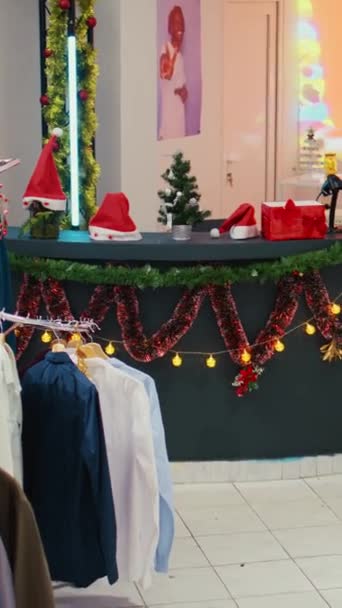 垂直视频吉布下来拍摄的节日时尚精品店装饰精美的圣诞树 花环和欢乐的圣诞数字屏幕 货架上有衣服的空商场商店 — 图库视频影像