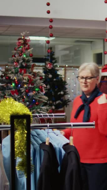 Вертикальне Відео Клієнти Катаються Навколо Магазину Одягу Прикрашеного Різдвяними Прикрасами — стокове відео