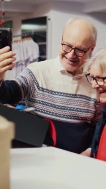 Şenlikli moda dükkanında kıdemli karı-koca dikey video görüntülerinde torunuyla çevrimiçi video görüşmeleri yapıyor ve ondan Noel aile etkinliğinden önce hediye olarak şık spor ceketleri almasını istiyor.