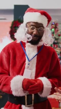 Noel Baba kostümü giyen dikey video perakendecisi bayram neşesi yaymak için alışveriş merkezi giyim mağazasında. Xmas temalı takım elbiseli çalışan mutlu müşteri kırmızı giysisini gösteriyor