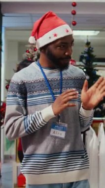 Noel 'de alışveriş merkezinin dekore edilmiş giyim mağazasında dikey video çeken eş ve eş, kış tatili promosyonları sırasında mükemmel kıyafetler bulan Afrikalı Amerikalı bir çalışan tarafından destekleniyor.