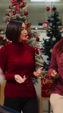Kış festivali temalı partisinde giyilecek kırmızı bluzla ilgilenen Asyalı dikey video müşterisi çalışanlara malzeme ve fiyatları soruyor. Noel kutlamaları için kostüm isteyen bir müşteri.