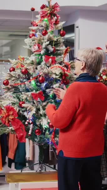 Xmasの垂直ビデオ従業員は サンタクロースの衣装を着てファッションブティックを飾り 冬の休暇シーズン中に衣料品店で美しく装飾されたクリスマスツリーの周りに集まりました — ストック動画