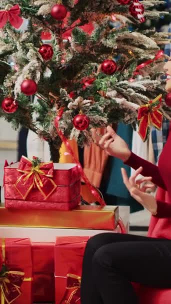 お祝いのクリスマスショッピング体験中にサンタクロースを偽装する従業員との会話に従事する垂直ビデオアジアの女性 ファッションショップの従業員からXmasプレゼントを受け取る顧客 — ストック動画