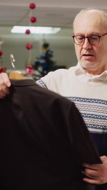 Verticale Video Oudere Man Onderzoekt Elegante Blazers Drukke Bruisende Winkel — Stockvideo