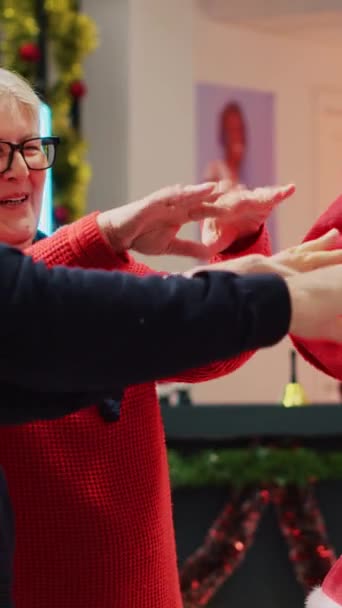 クリスマスラッフルホールドに参加する垂直ビデオクライアントのお祝いの衣料品店でサンタクロースとして服を着た小売アシスタント ラッキーな高齢者のカップルは プロモーションに勝った後に興奮しました — ストック動画