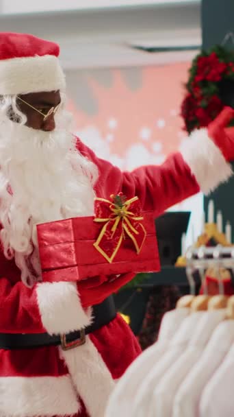 垂直录像零售助理在圣诞装饰品时装店模仿圣诞老人 邀请顾客参加圣诞抽奖比赛 以赢得冬季促销奖品 — 图库视频影像