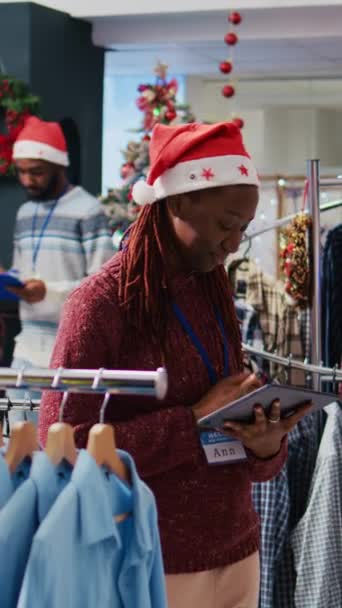 Vertikales Video Afrikanisch Amerikanischer Manager Mit Weihnachtsmütze Blättert Durch Kleiderständer — Stockvideo