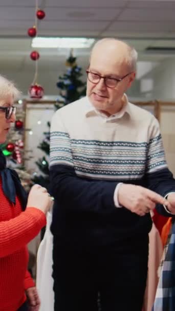 Vertical Video Tracking Shot Elderly Couple Browsing Shirts Festive Decorated — Stock Video