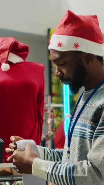 在圣诞装潢服装店 垂直录像经理戴着圣诞礼帽 为顾客安排正式的服装领结 主管在寒假期间视察圣诞装潢店的橱窗 — 图库视频影像