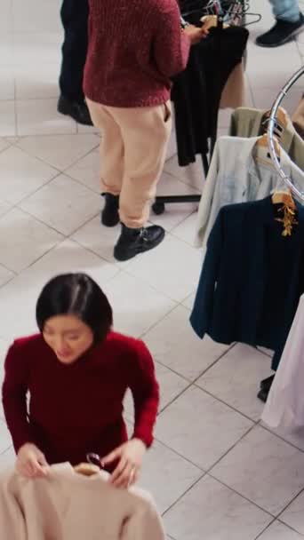 忙しいショッピングモールの衣料品店の通路を歩き回っている顧客の垂直ビデオトップダウンビューは クリスマスプロモーションセールイベント中に家族や友人のための贈り物として服を購入しようとしています — ストック動画