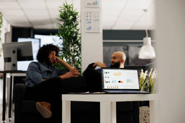 stock image Stock market investment revenue statistics report on laptop screen in office. Arab business company employees sitting on couch in coworking space and discussing financial analytics