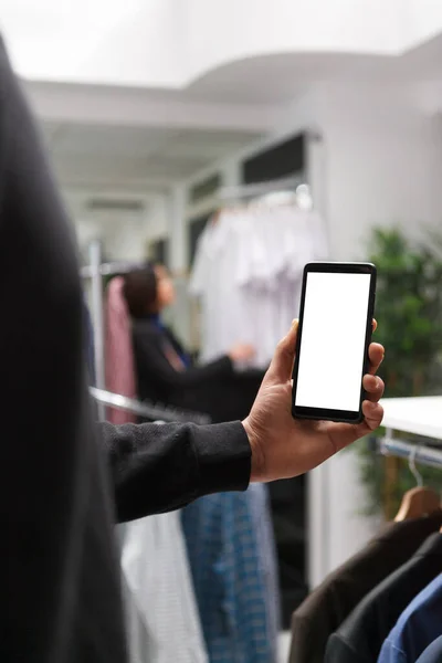 利用可能なアパレルオプションをチェックしながら 携帯電話の空白のデジタルディスプレイを使用して小売店の顧客 スマートフォンの空白のタッチスクリーンを示すショッピング モールのブティックの顧客 — ストック写真
