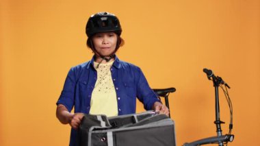 Kurye kadın müşteriye pizza getiren turuncu stüdyo arka planında izole edilmiş. BIPOC bisiklet sürücüsü müşteriye sipariş veriyor, termal sırt çantasından fast food kutuları çıkarıyor
