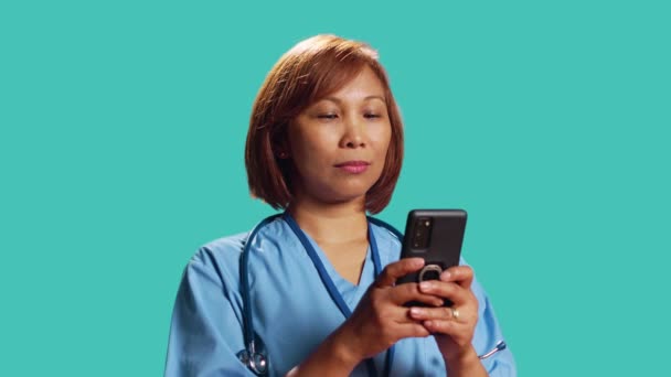 关闭快乐的诊所员工在工作时通过电话发短信 享受休息 乐观的Bipoc护士身穿职业制服 在网上与朋友聊天 在工作室背景上被隔离 — 图库视频影像