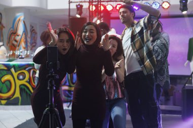 Bir grup neşeli arkadaş gece kulübünde parti yaparken akıllı telefondan tripodla fotoğraf çekiyorlar. Çeşitli genç erkek ve kadınlar cep telefonundan diskotek yayınlıyorlar.