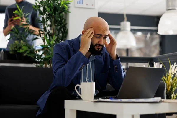 アラブの起業家は ノートパソコンのプレゼンテーションで働いている間に片頭痛に苦しんでいます コワーキングスペースにおける頭痛計画マーケティング戦略を持つ若手企業経営責任者 — ストック写真