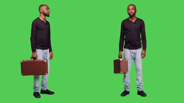 カメラにスーツケースの荷物を抱えて何かを待っているカジュアルな人は 緑の画面の背景の上に立っている 若いです男でブリーフケースを運ぶ荷物でスタジオ 優しい大人 — ストック写真
