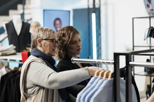 ショールームの従業員は トレンディな服を選択する高齢女性を支援し 現代のブティックでファブリックを議論します カジュアルウェアのためのシニアクライアントショッピング 衣料品店でファッショナブルな商品を購入 — ストック写真