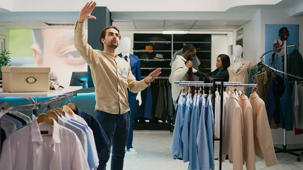 Store manager working with augmented reality hologram in shopping center, looking at modern trendy clothes on hangers. Retail worker using artificial intelligence in boutique, small business.