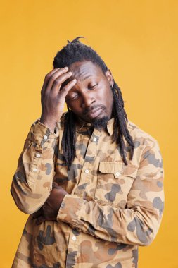 Kafası karışmış bir adam iş fikirleri üretiyor, zor iş sorunlarını çözmek için çözüm düşünüyor. Düşünceli Afro-Amerikan yetişkin, kararsız bir ifadeyle, sarı arka planda stüdyoda duruyor.