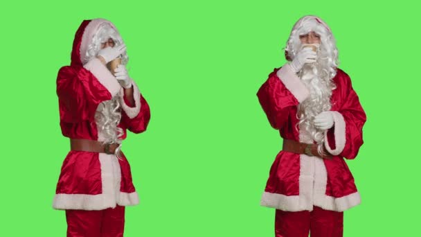 セントニックのキャラクターはスタジオでコーヒーを飲み カップでホットドリンクを楽しんで サンタクロースを白いひげで描いています 父親のクリスマス お祝いの飲み物として服を着た若い大人 — ストック動画