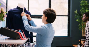 Çalışan kapanış düğmeleri, modern butikte şık ürünler düzenlemek. Mağazada çalışan beyaz bir yönetici alışveriş merkezindeki yeni moda koleksiyonlarıyla dolu askıları kontrol ediyor.