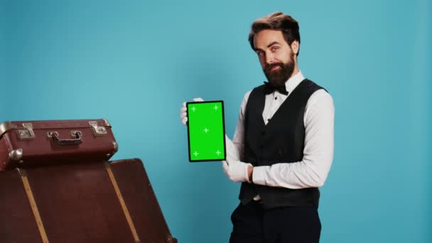 Portier Pozuje Zieloną Tabliczką Przed Kamerą Stojąc Obok Niebieskiego Tła — Wideo stockowe