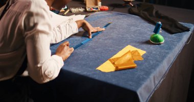 Atölyedeki metreyi kullanarak kumaş boyutlarını kontrol etmek için ölçüm bandıyla çalışan tasarımcı. Kadın tasarımcı modern moda ürünleri, küçük işletmeler tasarlamak için kıyafet hazırlıyor..