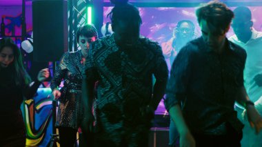Afrika kökenli Amerikalı DJ radyoda müzik yapıyor, kulaklık takıyor ve gece kulübündeki ses ekipmanlarında elektronik seslerle eğleniyor. Genç bir kadın bir grup insanla takılmaktan hoşlanıyor..