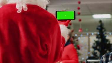 Noel Baba kostümü giyen, yeşil ekranlı telefon tutan, iş vardiyasına ara verip krom ekranda video izleyen, Noel Baba kostümlü bir çalışan.