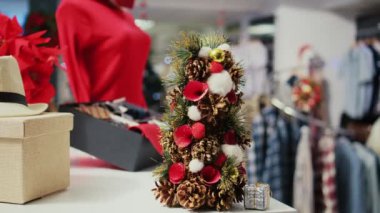 Kıyafet mağazasının masasında şık kravatların yanında duran çam kozalaklarından yapılmış minyatür Noel ağacının yakın çekimi. Boş moda dükkanında Xmas dekorasyonu