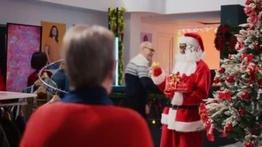 Noel Baba 'yı taklit eden neşeli bir adamın alışveriş merkezindeki giyim mağazasında çekilmiş bir fotoğrafı. Noel temalı moda mağazasında Noel çanları çalan ve yaşlı müşterilerle sohbet eden denetçi.