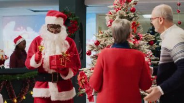 Noel Baba gibi giyinmiş Afrikalı bir işçi Noel çanı çalıyor ve güzel dekore edilmiş Noel ağacının yanında Xmas mağazasından alışveriş yapan yaşlı çiftle konuşuyor.