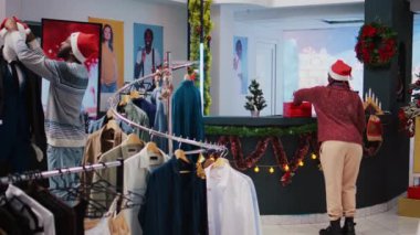 Afro-Amerikan iş arkadaşları alışveriş merkezinin giyim mağazasında Noel süslemeleri yapıyorlar. Çalışanlar şenlik havasında, moda butiği kostüm ile süsleniyor.