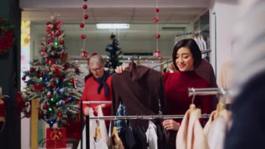 Bir kadın Noel için kıyafet mağazasında kıyafet karıştırıyor. Yeni yıl partisi için mükemmel kıyafetler arıyor. Moda mağazasının müşterisi ideal kıyafet arıyor.